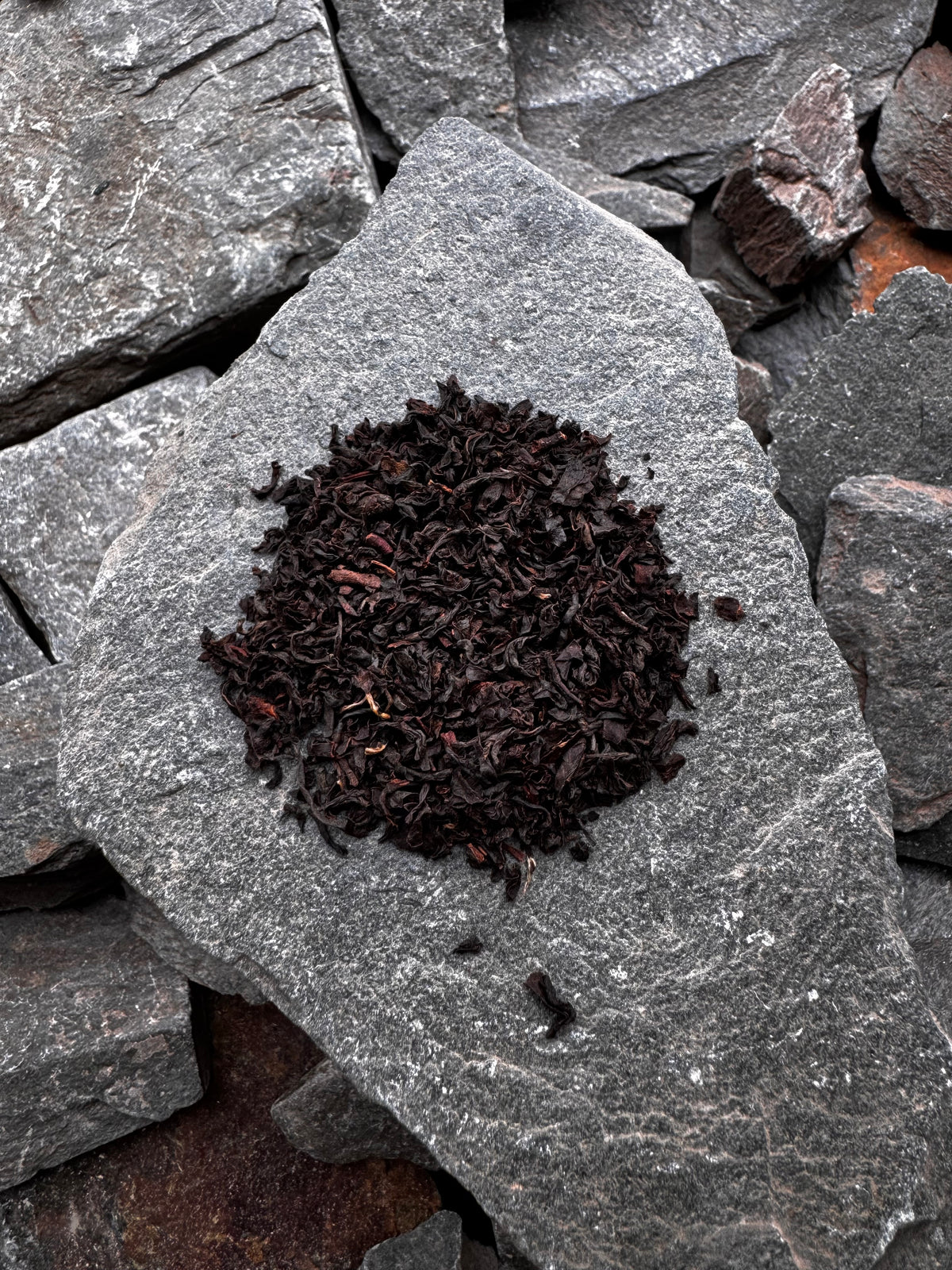 A mound of High Summit Tea Co. English Breakfast loose leaf black tea on a grey slate slab, surrounded by pieces of slate