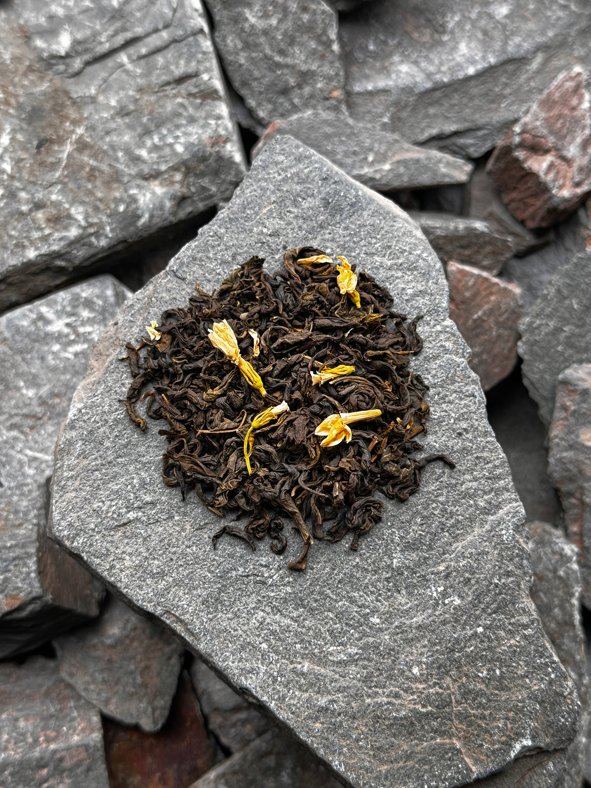 Jasmine with Flowers loose leaf green tea with visible yellow flower blossoms and petals, arranged on a grey slate stone at High Summit Tea Co.