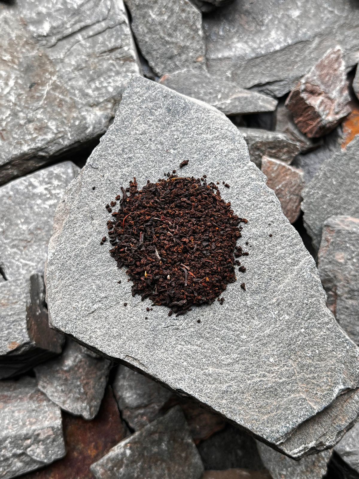 A small mound of The Lakes Blend loose leaf tea on a grey slate slab, surrounded by pieces of slate.